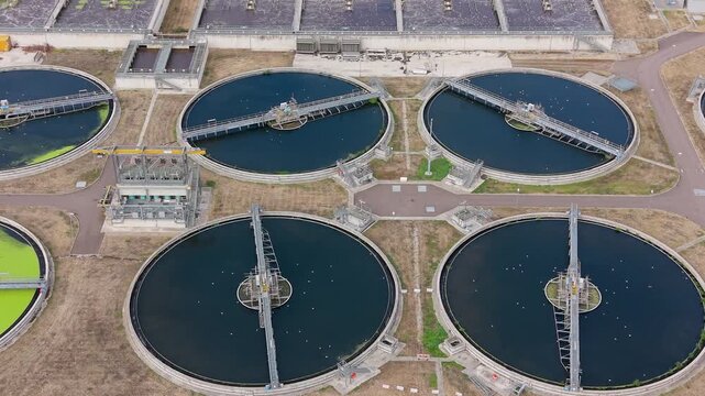 Water treatment clarifiers in Edmonton shown from above, right pan drone view over sewage works with circular settling tanks, dark basins and green algae patches on surface.