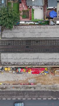 Leyton tube station renovation seen from above, aerial right pan shows new lift shafts and footbridge steelwork over rail tracks, fenced storage areas and building materials. Vertical format.