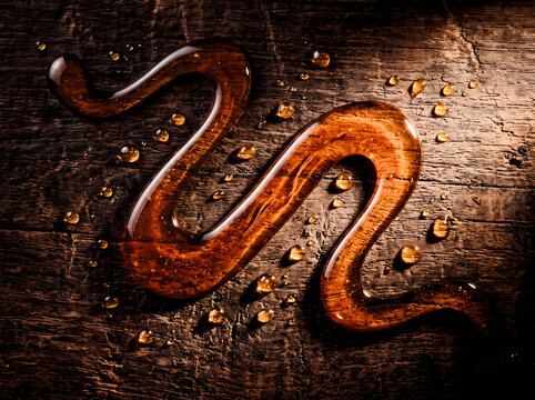 Golden honey syrup swirled in a wavy pattern with droplets on dark rustic wood