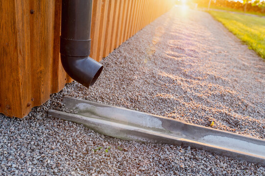Close-up of a plastic gutter on the corner of a building made of metal siding and a cement drainage channel