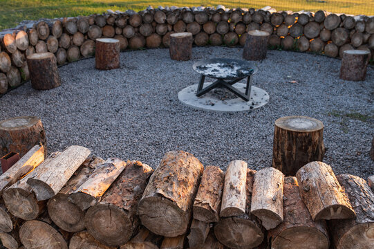 Round stone firepit surrounded by log seating in outdoor recreation area with evening string lighting