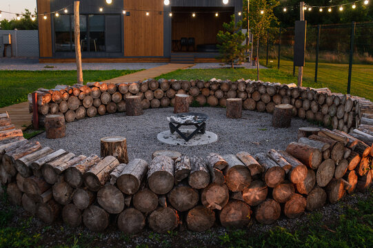 Rustic outdoor firepit built from stacked logs and natural stone with central fire bowl in landscaped backyard and lanterns
