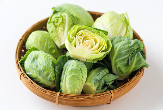 Close-up of a bunch of baby cabbages in a woven basket, arranged on a clean white background.