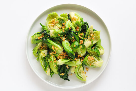 Top view of saut&eacute;ed baby cabbage garnished with golden fried garlic bits on a clean white dish.