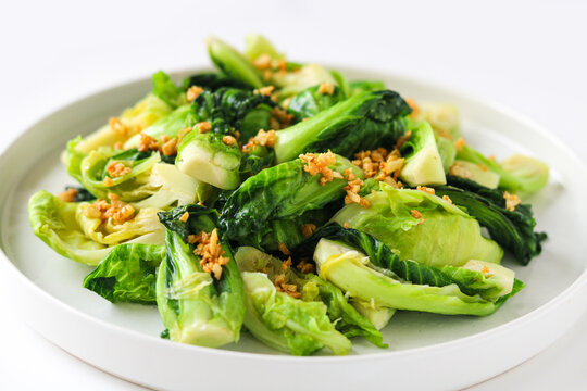 Close-up view of saut&eacute;ed baby cabbage garnished with golden fried garlic bits on a clean white dish.