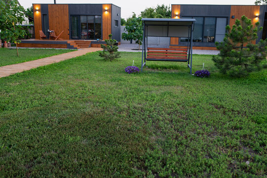 Garden swing, gazebo near the house for relaxing on the lawn. Siding-clad house and countryside getaway, rental property, view from a distance, large open lawn area.