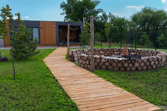 A cozy vacation cottage featuring modern materials, metal siding, and a flat roof, complete with a lawn, a wooden walkway, and a fire pit area. Outdoor recreation, holiday retreat.
