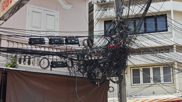 Messy and tangled overhead internet and communication cables on a concrete power pole.