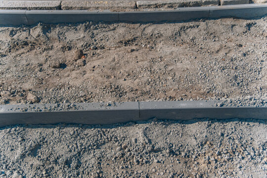 Top view of gravel and sand foundation prepared between installed concrete curb borders during sidewalk construction