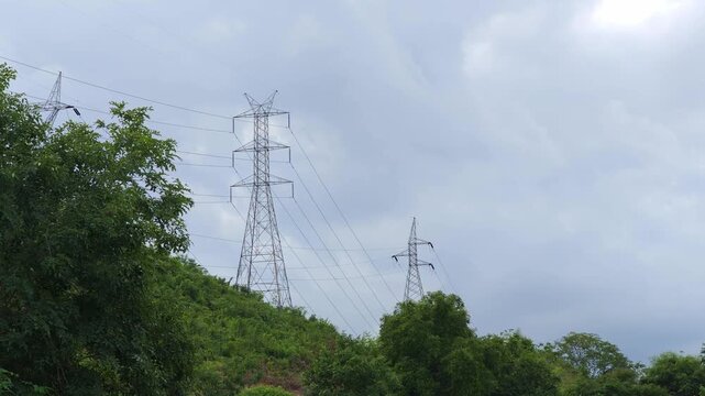 : High voltage electricity transmission towers standing on a mountain ridge, surrounded by a natural landscape under daylight.