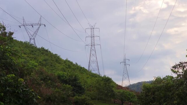 : High voltage electricity transmission towers standing on a mountain ridge, surrounded by a natural landscape under daylight.