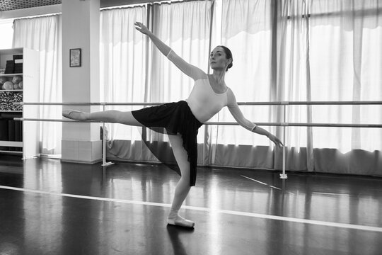 Young female ballerina balances in ballet studio under soft monochrome light