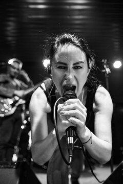 Adult female singer belting into microphone during sound check under monochrome stage lights
