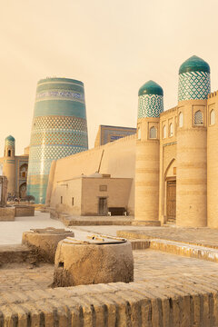 Kalta Minor minaret and twin-domed gate in Ichan Kala, Khiva, bathed in warm golden light. Historic Uzbekistan landmark with turquoise tilework and mudbrick walls, ideal for travel and heritage.