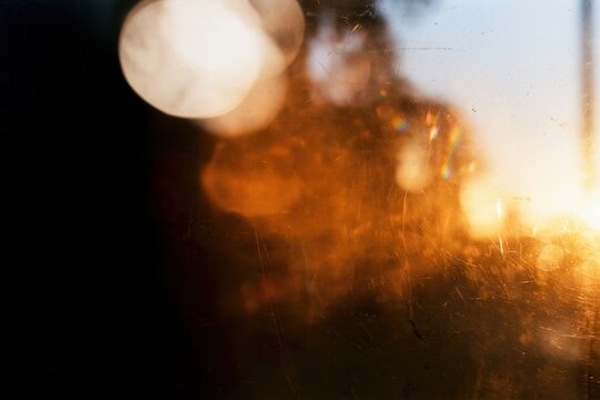 Warm orange light leak with soft bokeh glow on dark distressed film texture, abstract vintage analog background with grain, dust and atmospheric blur