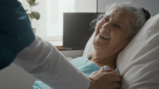 Senior woman patient lying in hospital bed smiling while doctor comforting her with supportive touch. Clip ideal for geriatric healthcare promotions and medical care marketing