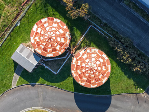 Aerial view of two large circular industrial storage tanks with weathered, rusted metal roofs at the Rowville Factory, surrounded by grass and paved roads in Melbourne, VIC, Australia.