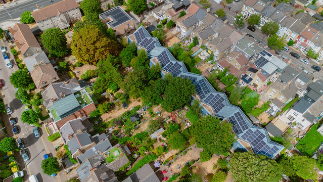 Aerial view of a unique zig-zag shaped building with solar panels surrounded by lush trees and residential houses in London, England, United Kingdom.