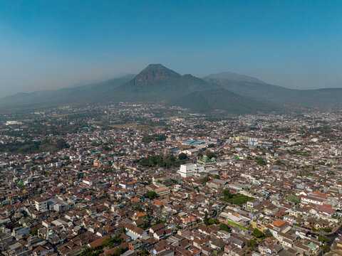 Aerial view of the city of Batu with Mount Panderman rising in the background, featuring dense residential rooftops and urban infrastructure in Batu, East Java, Indonesia.
