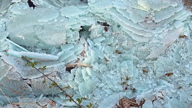 Smooth camera push-in shot towards a massive pile of broken tempered safety glass shards and cracked layers outdoors. Close-up of shattered turquoise glass structure.