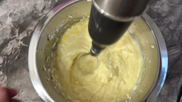 Hand blender whips fresh cream to soft peaks in a tall mixing bowl, smooth, airy, and glossy, for dessert or cake, a candid authentic life baking ritual.