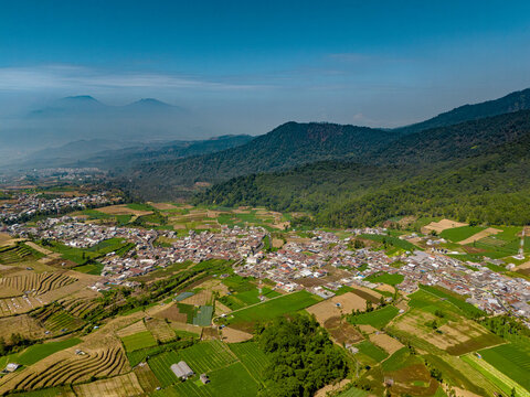Aerial view of Brakseng farmland and village nestled among lush green terraced fields and rolling mountains in Batu, East Java, Indonesia.