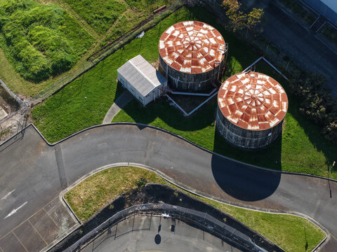 Aerial view of Rowville Factory featuring two large circular storage tanks with rusty roofs next to a small building, surrounded by lawns and asphalt roads in Melbourne, VIC, Australia.