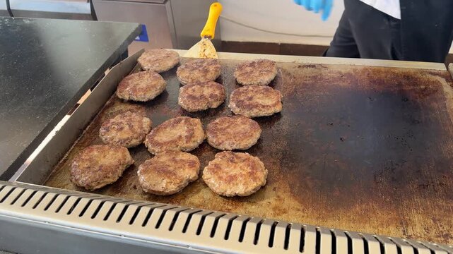 Fast food cafe, twelve patties frying on grill, sizzling meat, busy kitchen, cooking burgers.