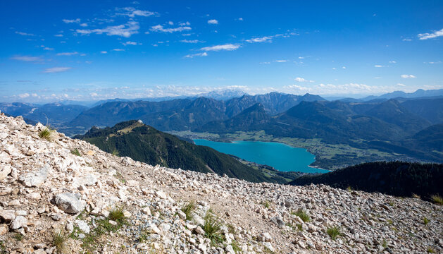 Scenic mountain landscape overlooking a bright turquoise lake with green valley and distant blue mountains under a cloudy sky