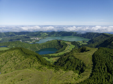 Aerial view of Sete Cidades volcanic crater lakes surrounded by lush green hills and forests under a clear blue sky in the Azores, Portugal.