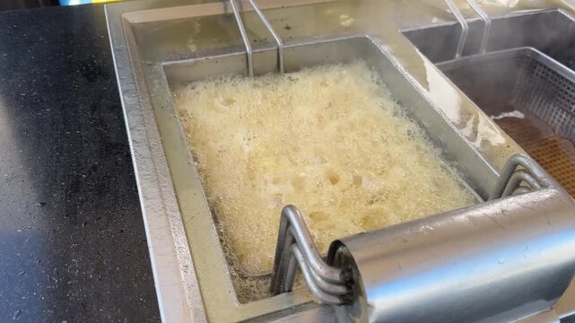 Deep fryer with French fries and boiling oil, bubbling golden potatoes, crispy fast food cooking process.