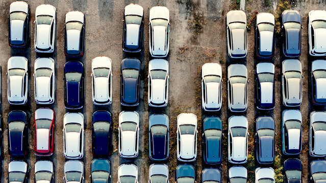 Aerial overhead of new cars and SUVs parked closely in rows at an outdoor lot. Representing the automotive industry. Vehicle manufacturing. Global import and export logistics