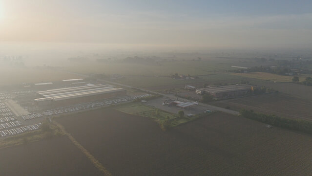 Aerial overlooking car yard with numerous SUVs and vehicles, manufacturing facility, logistics hub, gas station, and commercial trading operations in a misty, foggy landscape