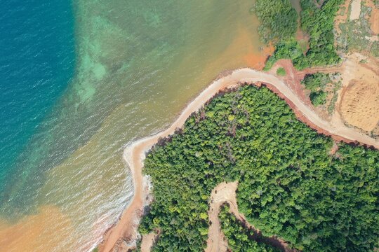 Aerial view of the PT Ceria Nugraha Indotama mining site coastline, showing sediment-laden water meeting the sea, with lush forest and dirt roads in Wolo, South East Sulawesi, Indonesia.