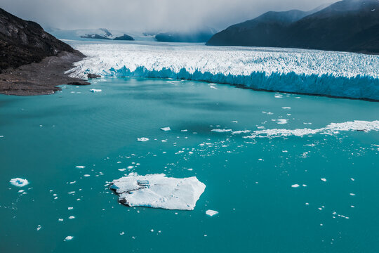 Aerial view of Perito Moreno Glacier with floating icebergs in the turquoise water and rugged mountains in the background in Perito Moreno, Santa Cruz Province, Argentina.
