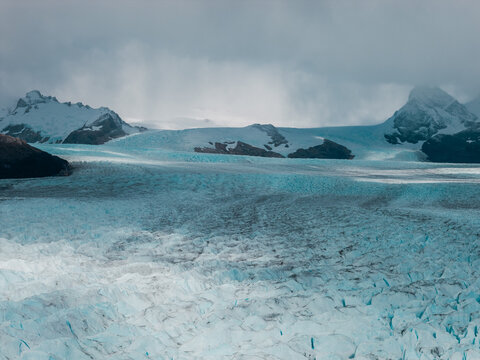 Aerial view of the massive blue ice formations and crevasses of the Perito Moreno Glacier surrounded by snow-capped mountains in Perito Moreno, Santa Cruz Province, Argentina.