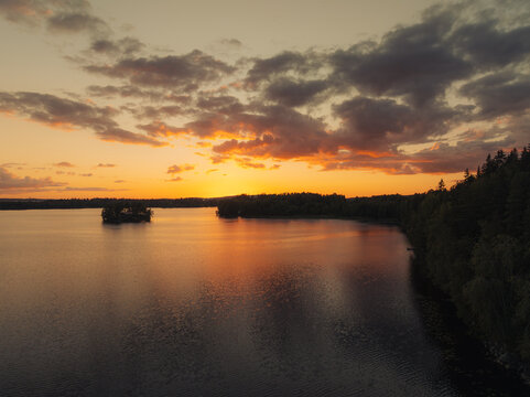 Aerial view of Nasijarvi lake at sunset with calm water, a small island, and surrounding forest under a dramatic golden sky in Tampere, Pirkanmaa, Finland.