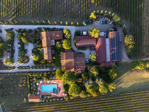Aerial view of a rural estate with a swimming pool, surrounding vineyards, and solar panels on the rooftops in Faenza, Emilia-Romagna, Italy.