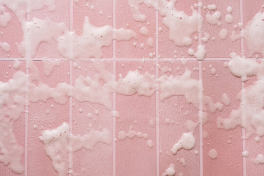 Scattered cleaning foam on pink tiles with straight grout lines in overhead view.