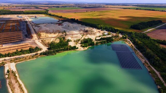 Aerial view of floating solar panels and sand quarry.. Drone captures an industrial excavation site with photovoltaic modules on a green artificial lake surrounded by fields.