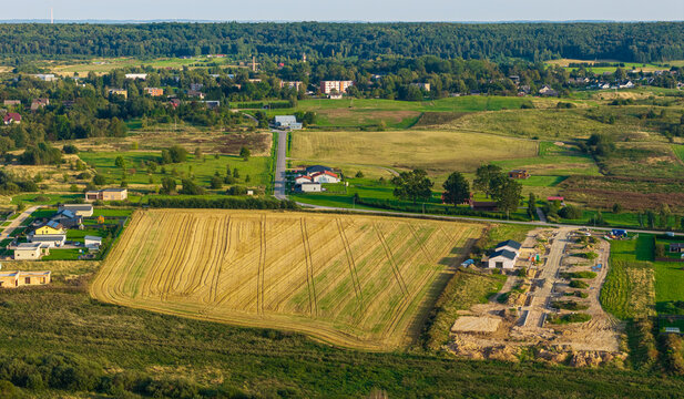 Aerial view of the rural landscape near Kaisiadorys, featuring harvested golden fields, scattered houses, green meadows, and a road network in Kaisiadorys, Kaunas County, Lithuania.