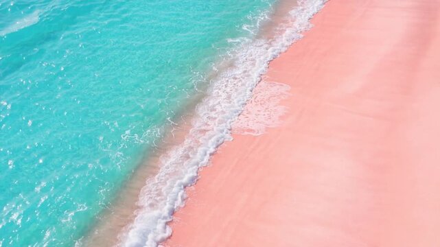 Aerial view of turquoise ocean waves gently washing onto a unique pink sandy beach shore