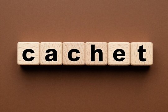 Wooden blocks with black letters spell cachet on brown background. Square timber cubes form word on table. Conceptual typography design for business prestige, status, reputation, social standing.