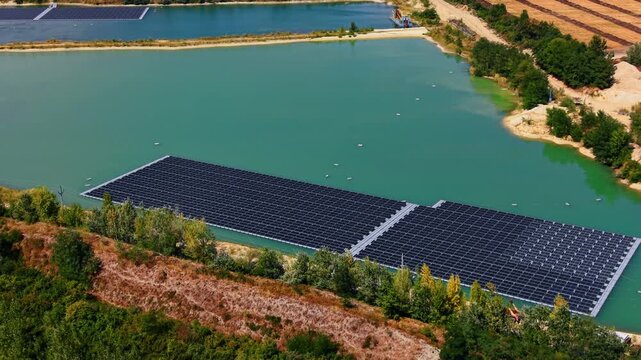 Close aerial view of photovoltaic array floating on green water. An anchored solar power plant operates on the surface of a former mining site bordered by trees and vegetation.