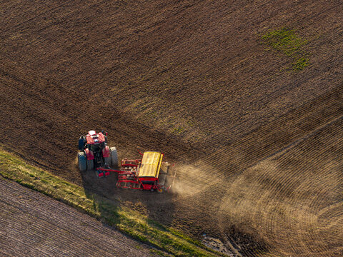 Aerial view of a red tractor pulling a yellow agricultural seeder through a large plowed field in Ziezmariai, Kaunas County, Lithuania.