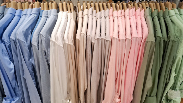 Neatly organized row of men long sleeve formal button down dress shirts hanging on wooden hangers in retail store clothing display
