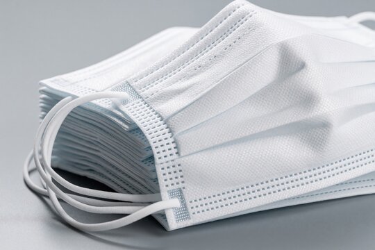 Stack of clean white disposable face masks on a grey background. These essential protective items offer safety against illness and pollution. Masks ensure personal hygiene and public health.