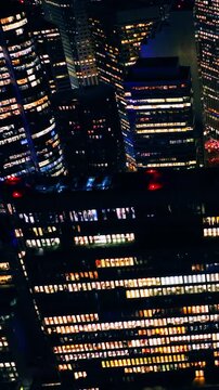 Overhead view of downtown high rise buildings, San Francisco, California. Rows of lit office windows glow gold and blue with red beacon lights on rooftops at night. Vertical video.