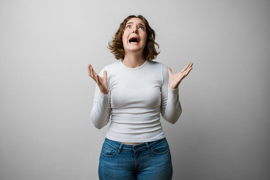 Woman casual expression, mad shouting, arms raised, crazy shout and yelling in frustration, aggressive pose against a white background