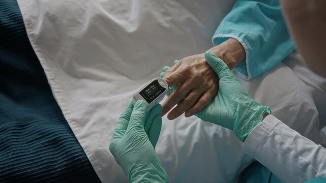 Unrecognizable doctor placing pulse oximeter on senior patient finger to monitor vital signs. Clip fits geriatric healthcare advertising, clinic promotions, and telemedicine projects